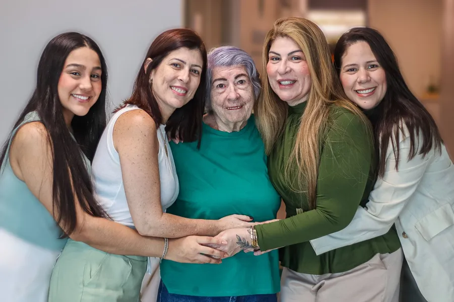 Suzana, a bisa de cabelos lilás, abraçada por Analice, Alice e as mulheres da família